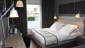 Una habitación de hotel moderna con una cama grande, dos lámparas de noche, un escritorio con cafetera y vistas a la ciudad.