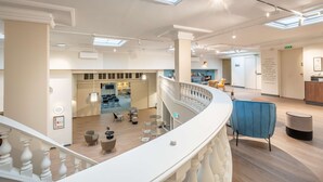 Un hall de hotel espacioso con una escalera central, un área de descanso con mesas redondas y vistas al comedor.