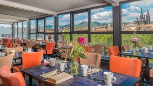 Restaurante con amplios ventanales que ofrecen vistas a un paisaje urbano y una catedral. Las mesas, con sillas y centros de mesa florales, están dispuestas.