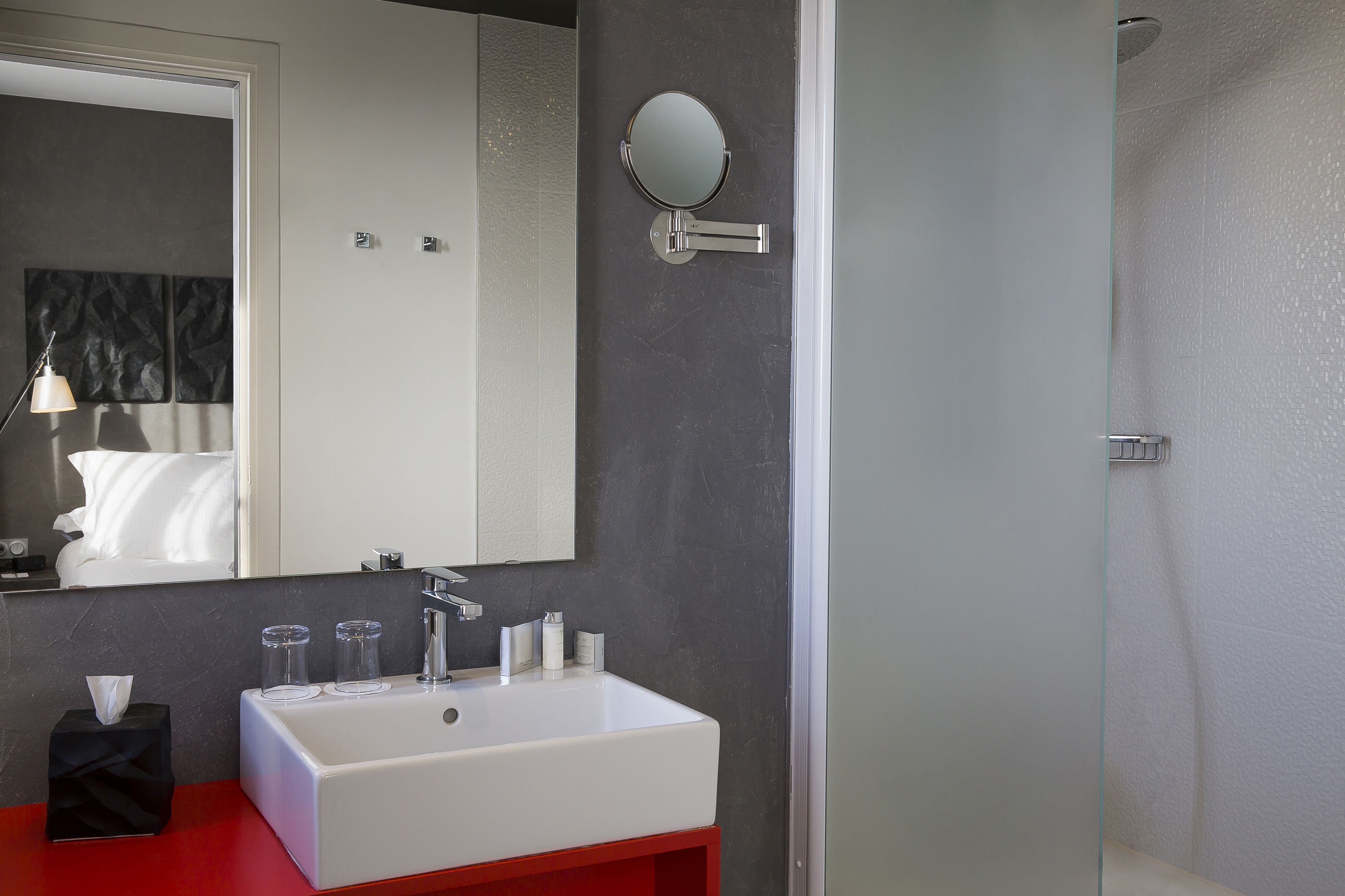 Ein modernes Badezimmer mit einem weißen Waschbecken, einem runden Spiegel und einer roten Kommode.