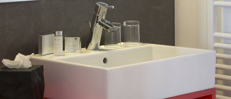 A modern bathroom with a white sink, chrome faucet, and a mirror above it. There are two clear glasses on the sink and a black tissue box on the counter.