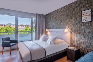 Une chambre d’hôtel avec un grand lit, une chaise, une table de chevet et une vue sur des immeubles et des espaces verts.