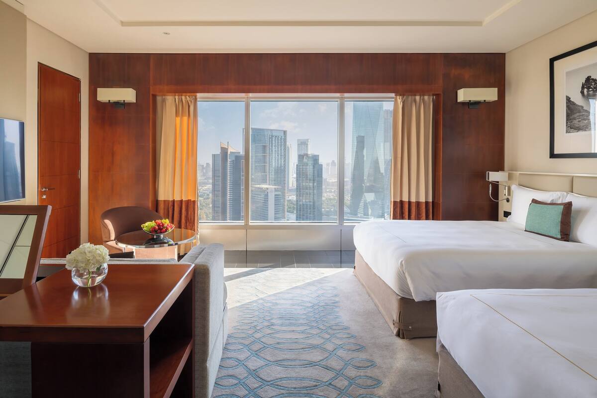 Habitación de hotel con vista a la ciudad, dos camas, un escritorio y una silla.