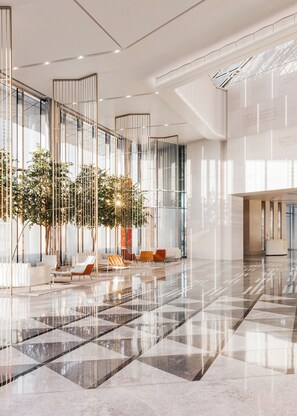 Un hall d’entrée spacieux, agrémenté d’un grand arbre, de sièges modernes et d’un sol réfléchissant.