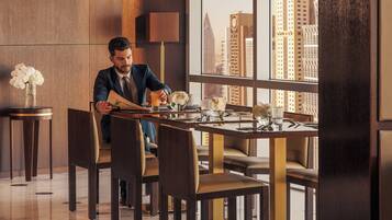 A modern hotel room with a dining area featuring a large window with a city view, a well-lit space, and a clean, contemporary design.