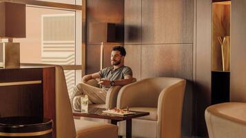 A modern hotel room with a large window, a sofa, a table with snacks, and a lamp.