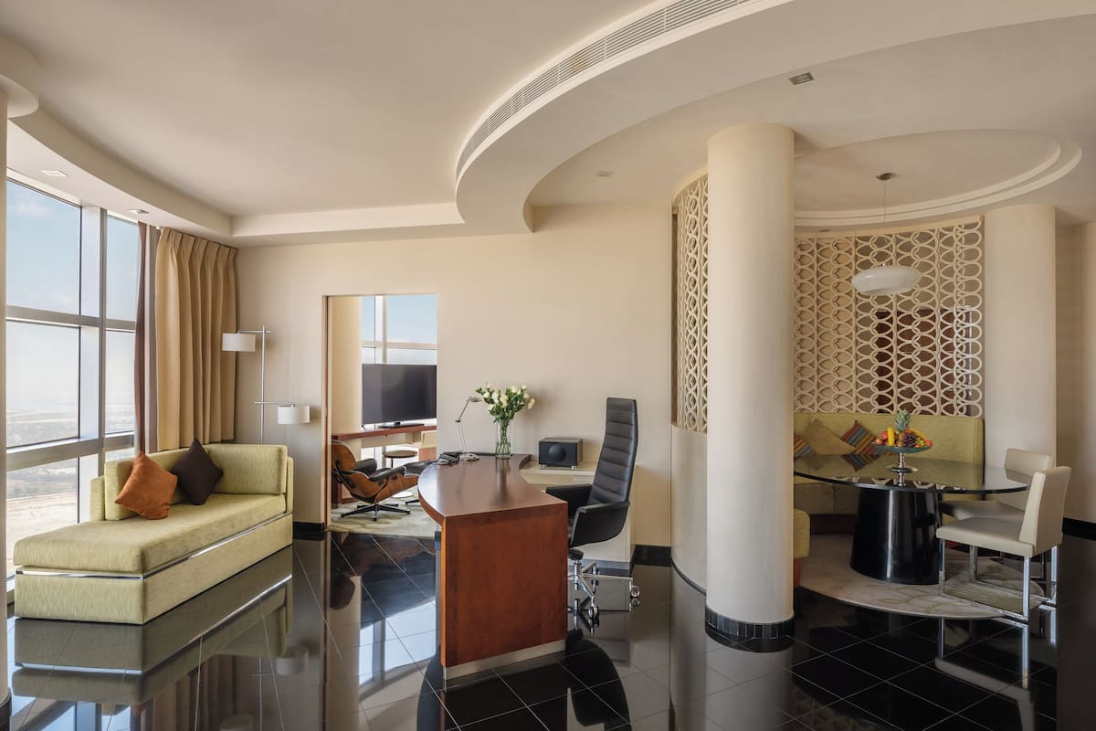 Una habitación de hotel moderna con sofá, escritorio, silla y mesa de comedor.
