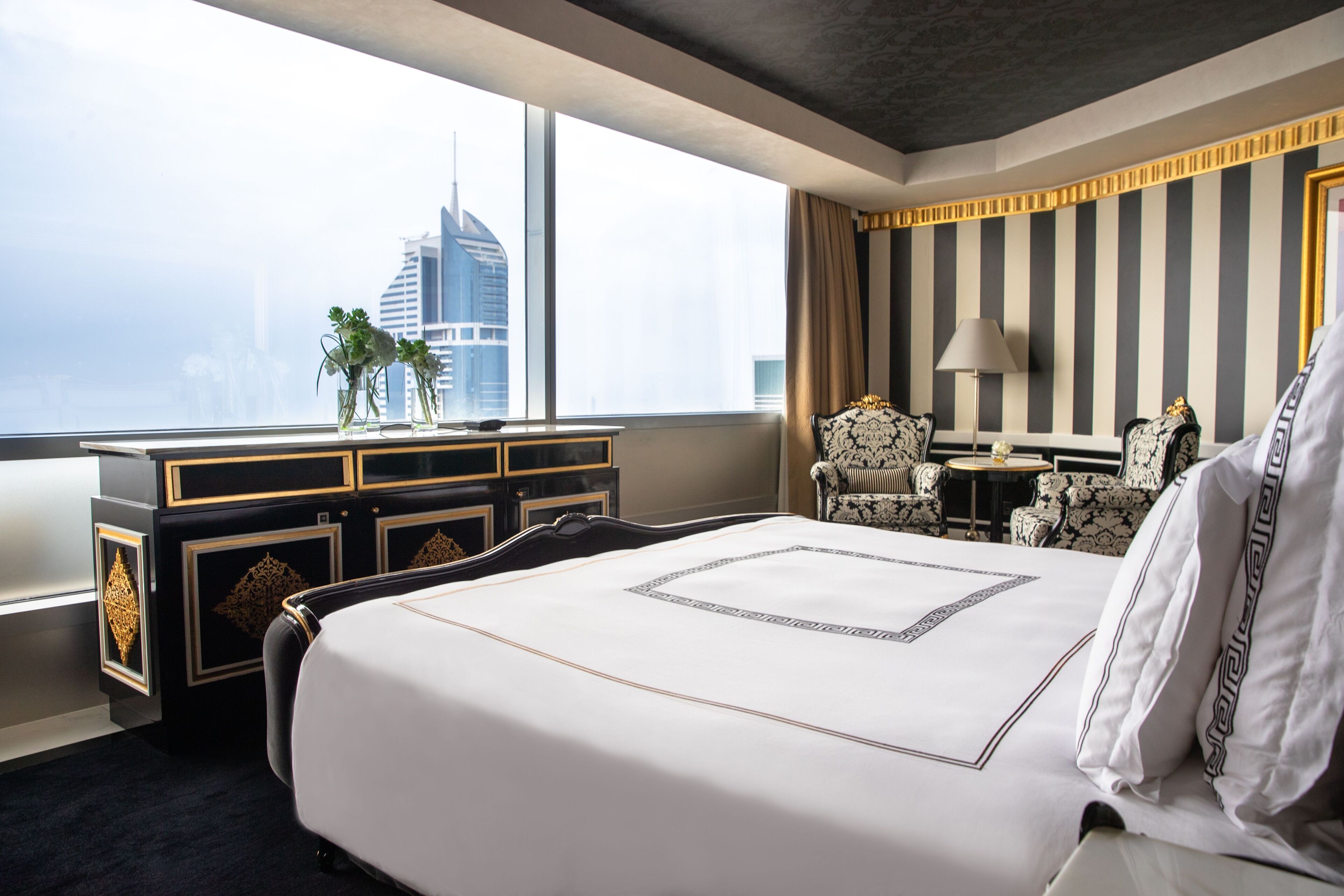A hotel room with a large bed, a desk, and a view of a city skyline.
