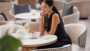 Une femme est assise à une table ronde, devant un plateau de desserts, une théière et une tasse.