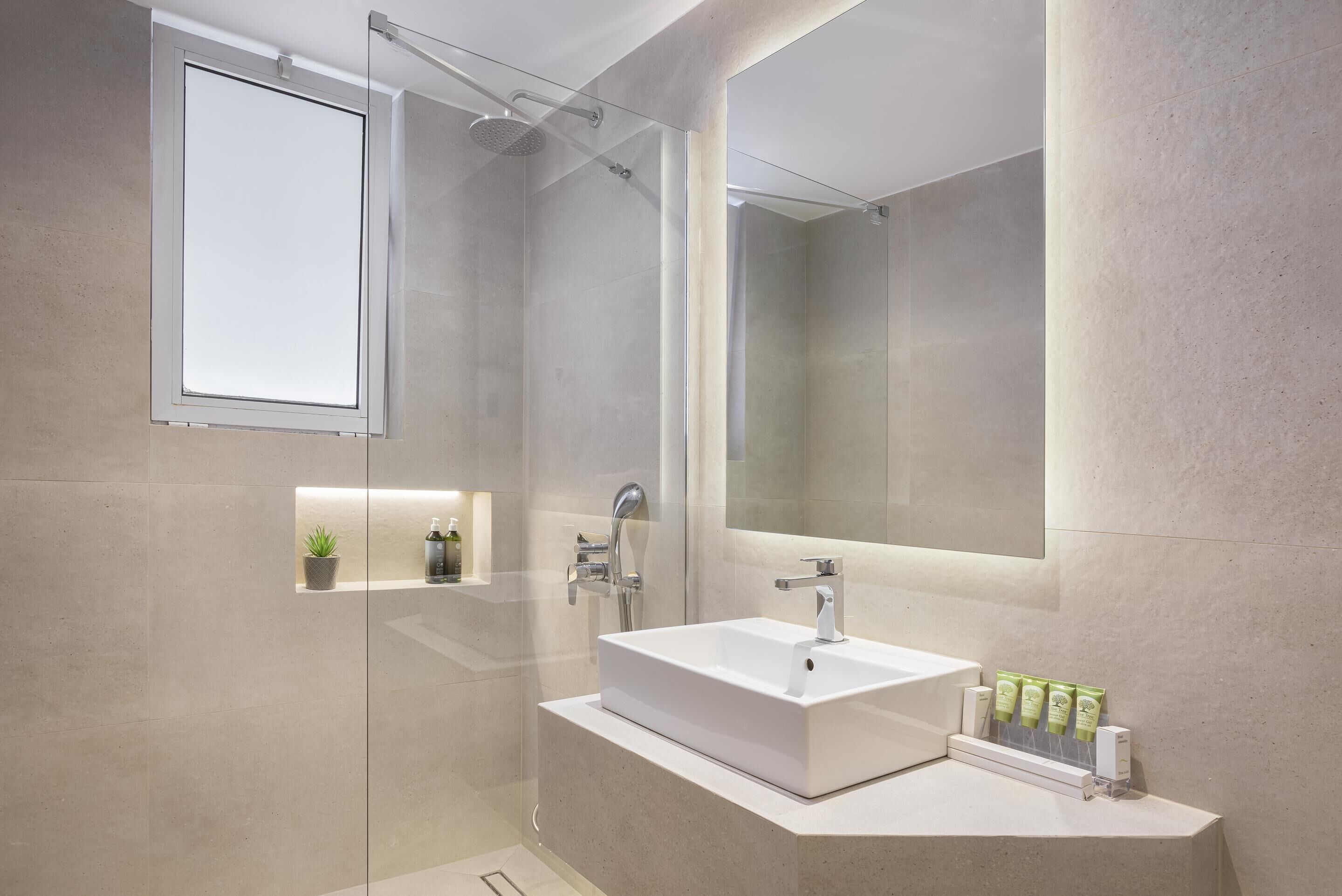 Un baño moderno con cabina de ducha de vidrio, un espejo grande y un lavamanos blanco con artículos de aseo.