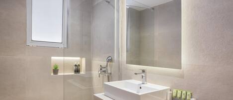 Un baño moderno con cabina de ducha de vidrio, un espejo grande y un lavamanos blanco con artículos de aseo.
