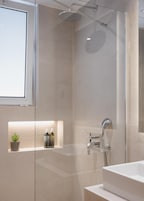 A modern bathroom with a glass shower enclosure, a built-in sink, and a small shelf with toiletries.