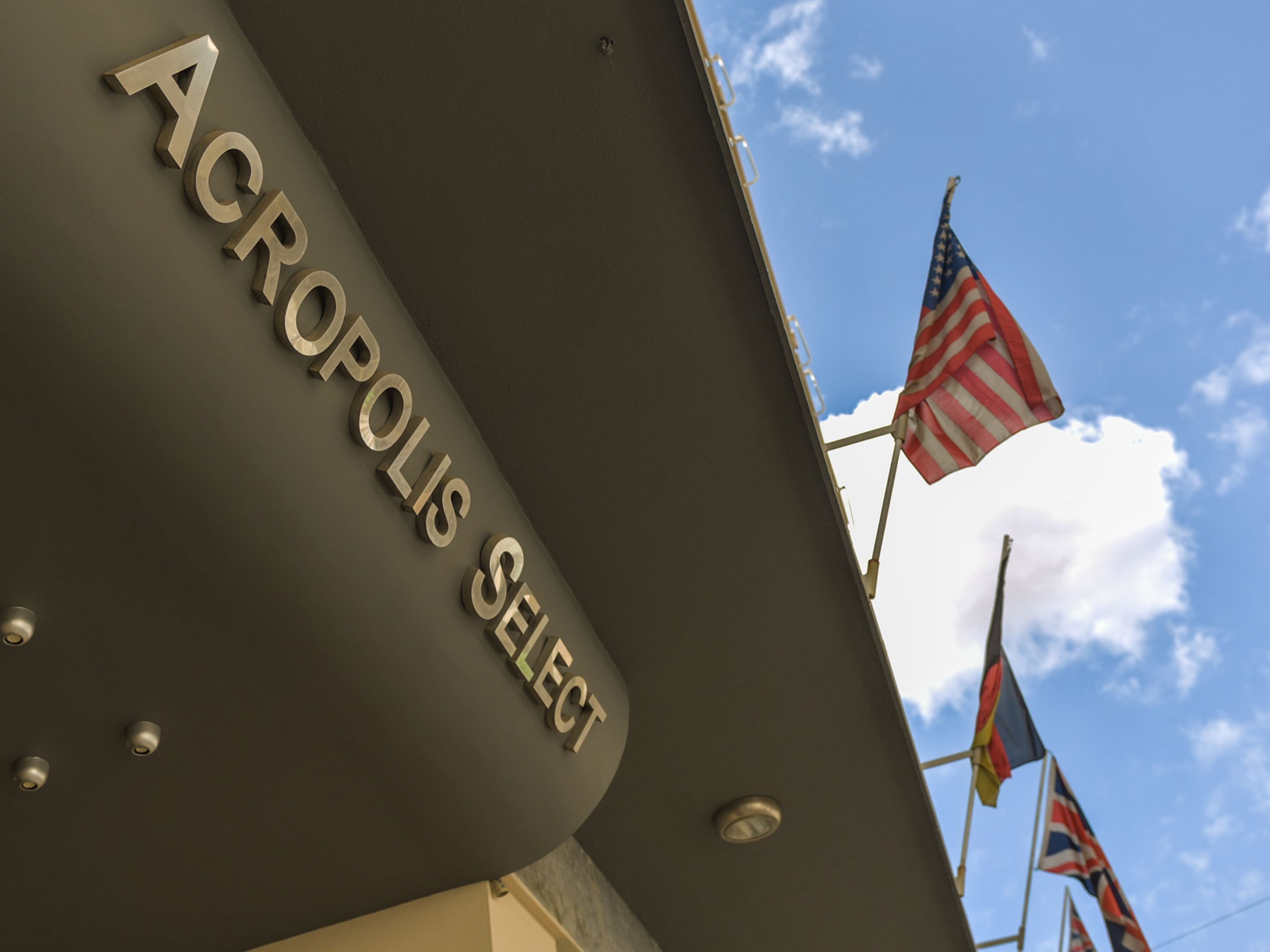 Een bord met de tekst 'ACROPOLIS SELECT' op een gevel, met Amerikaanse vlaggen op de achtergrond.