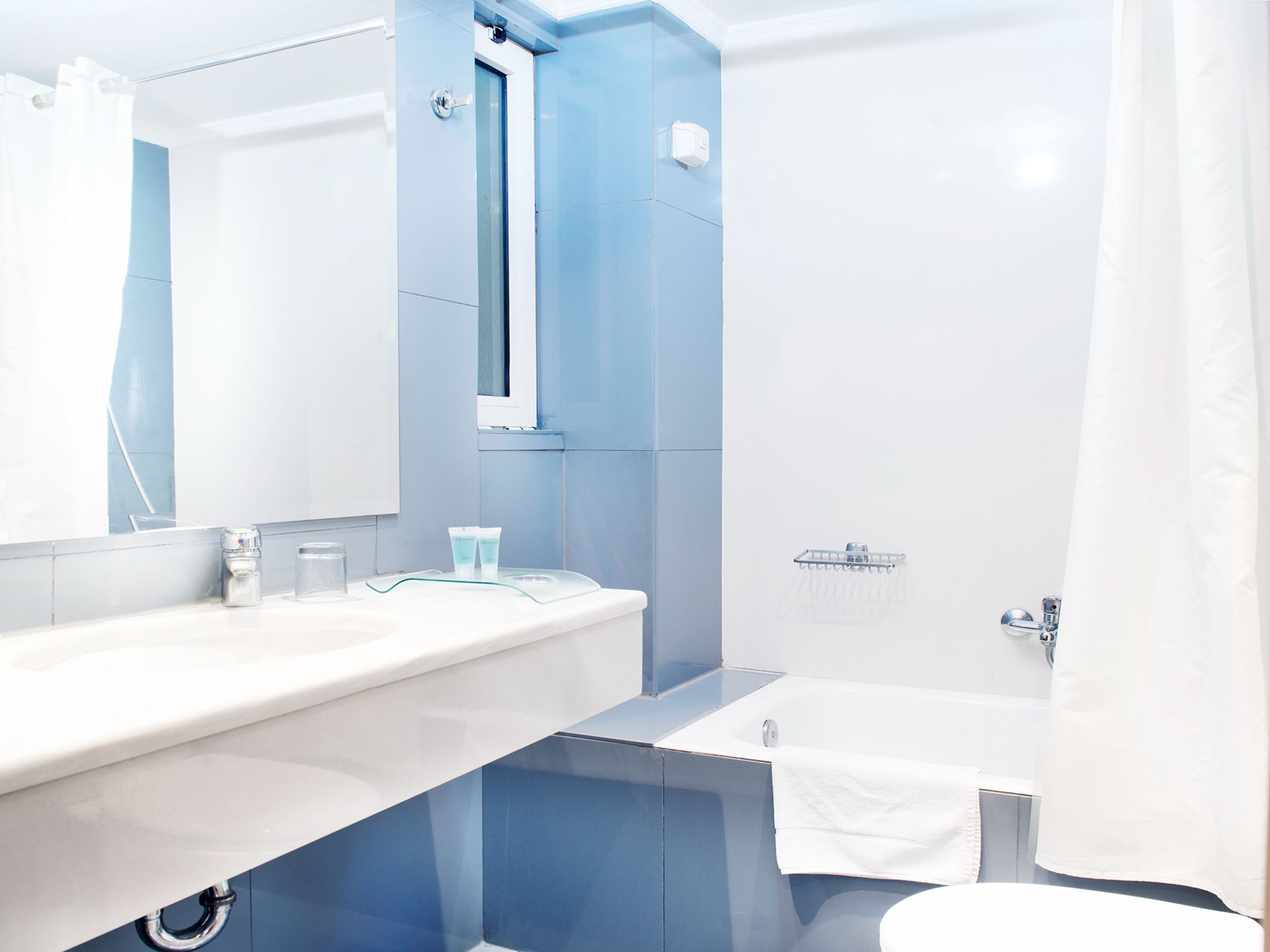 A modern bathroom with a white sink, blue walls, a mirror, and a shower area.