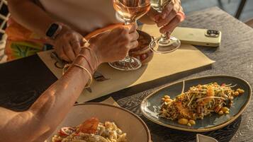 A dining table with a plate of pasta, a glass of wine, and a smartphone.