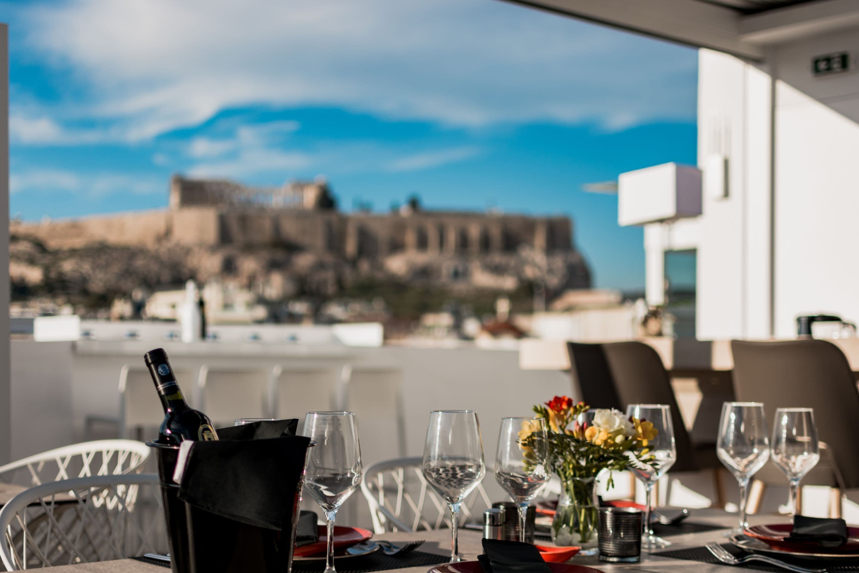 A dining table set with wine glasses, a bottle, and a vase with flowers, overlooking a historic fort.