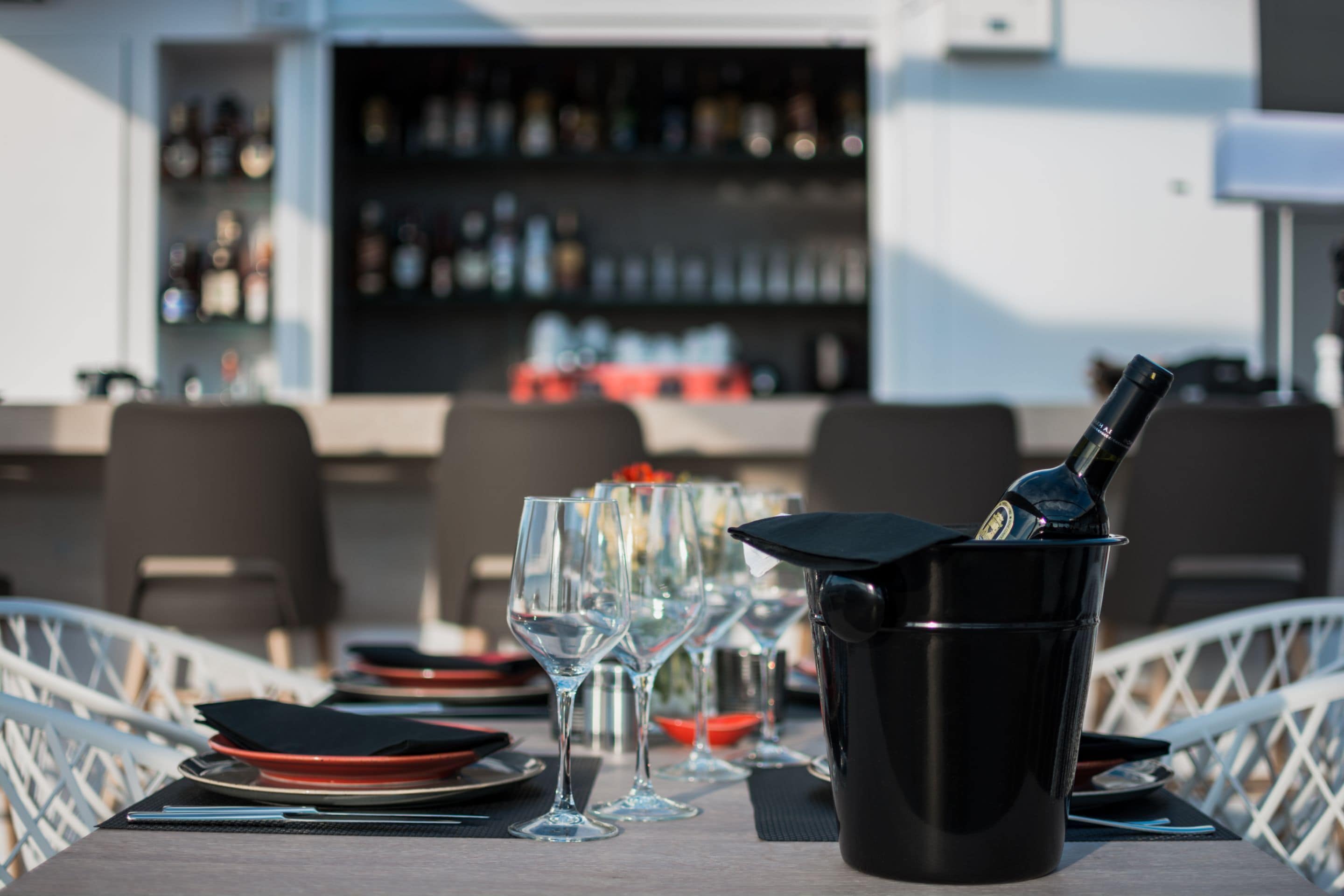 A table set with wine glasses, a black bottle in a holder, and red plates.