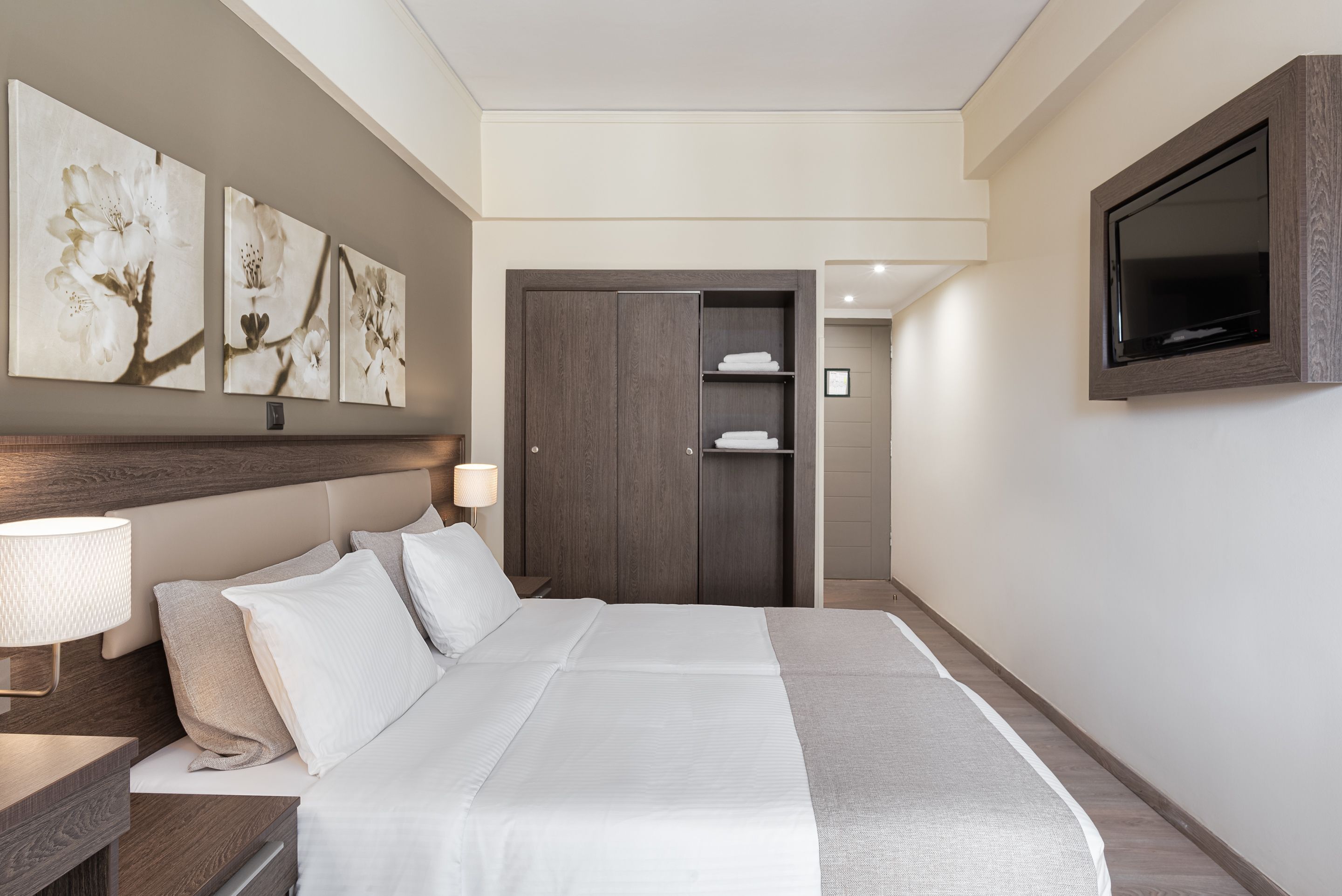 Ein Hotelzimmer mit einem großen Bett, einem Kleiderschrank, einem Fernseher und Wandbildern.