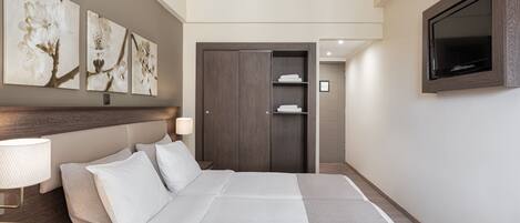 A hotel room with a large bed, a wardrobe, a television, and wall-mounted artwork.