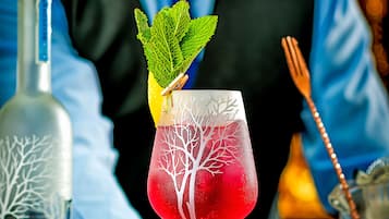Een bartender bereidt een cocktail voor, met een decoratief boomdesign op het glas, een fles Belvedere wodka en een klein schaaltje olijven.
