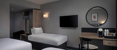 Habitación de hotel con dos camas, un escritorio, una silla, un televisor y una cafetera.