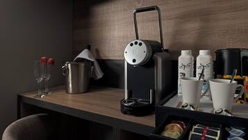 A kitchenette with a coffee maker, two cups, a kettle, and a coffee pod box.