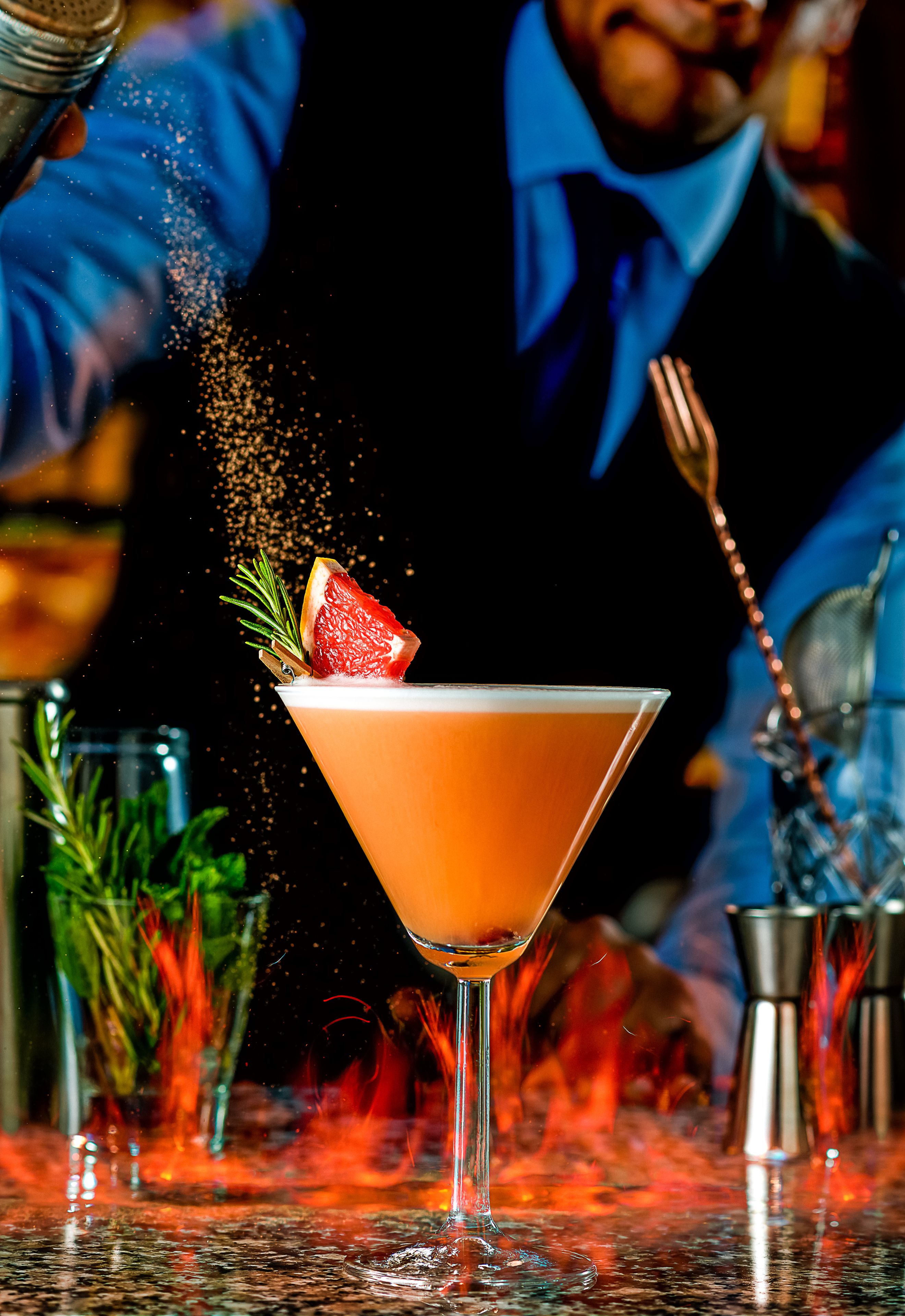 A cocktail being prepared with a garnish and a shaker in the background.