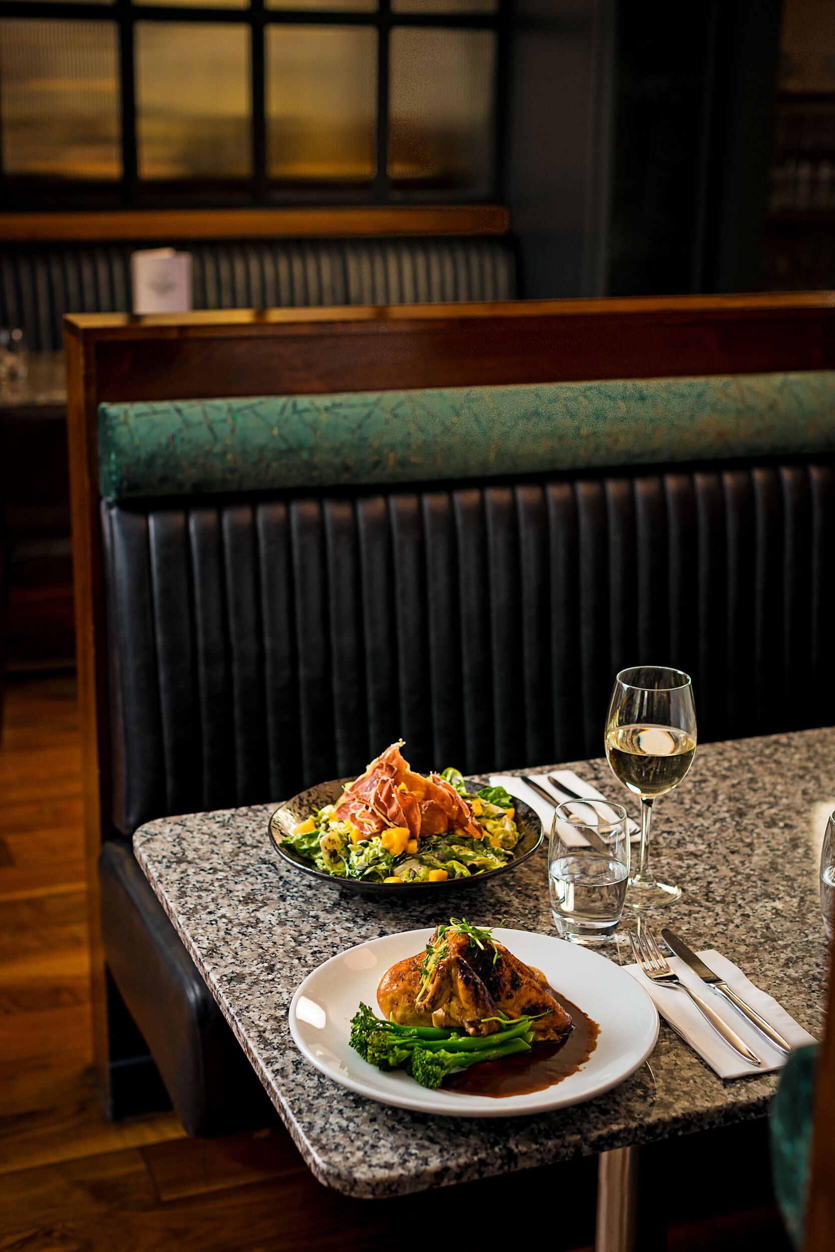 A restaurant setting with a table set for two, featuring a plate of food and a glass of white wine.