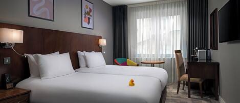 Habitación de hotel con una cama grande, mesitas de noche, un escritorio, una silla, un televisor y una ventana con cortinas.