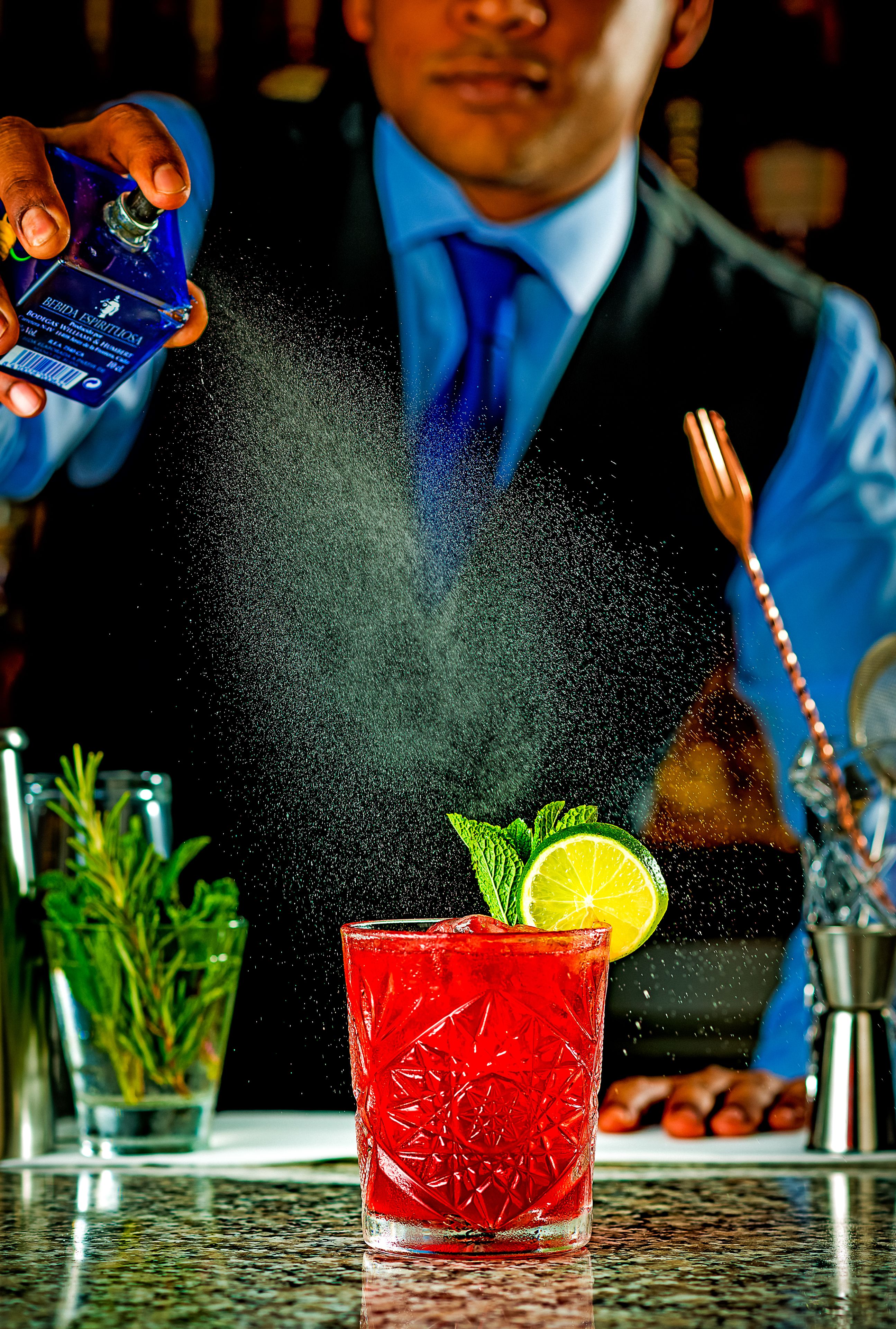 A bartender pouring a drink with a lime garnish into a red glass.