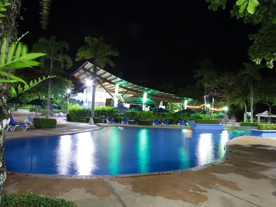 A nighttime pool area with a curved pool, lounge chairs, and a covered pavilion.