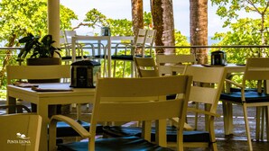 An outdoor seating area with white chairs and tables, a potted plant, and a view of the ocean. - Hotel Punta Leona (Tárcoles)
