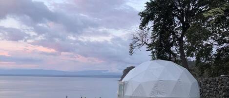 A geodesic dome structure with a view of a body of water and a cloudy sky.