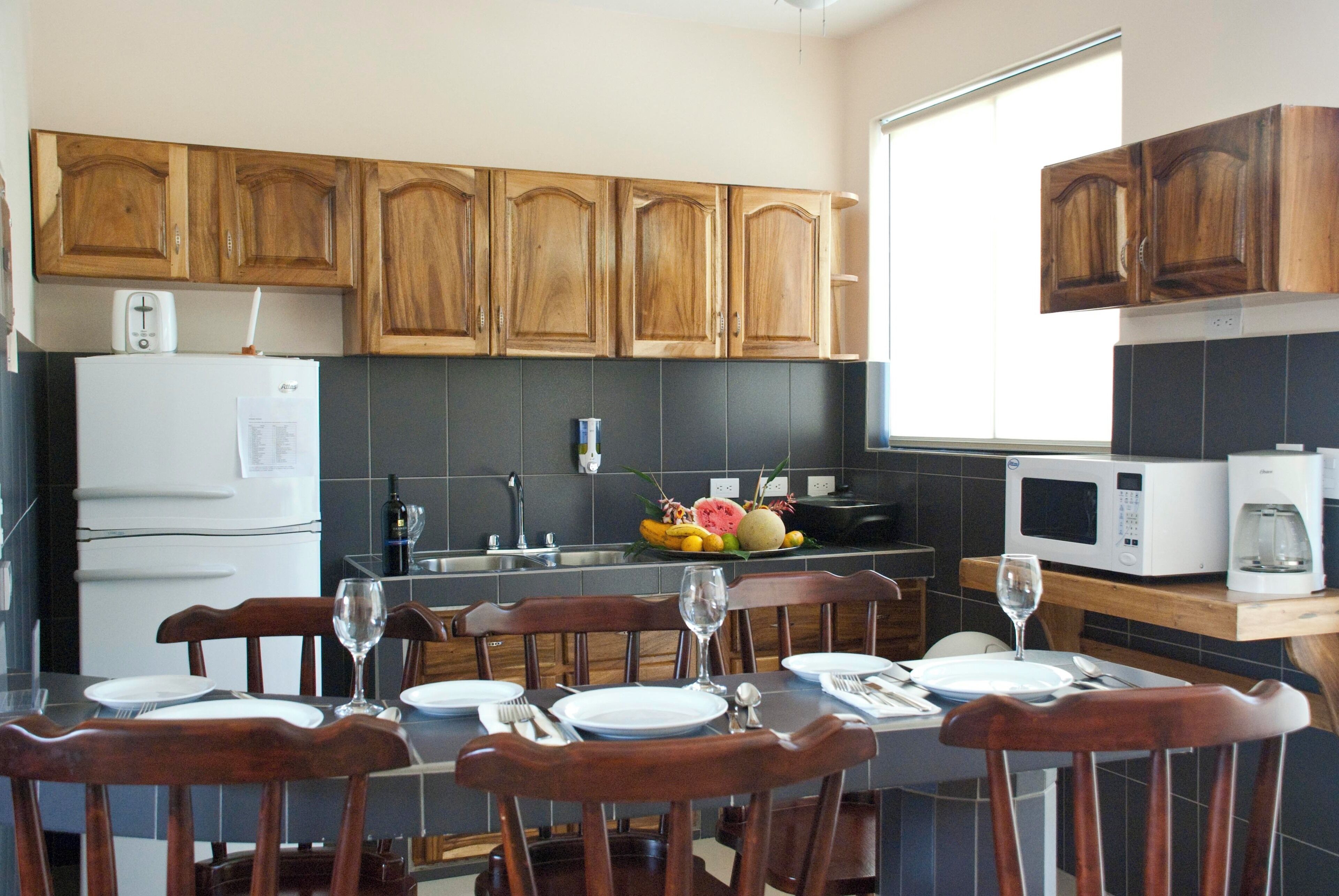 A kitchen with wooden cabinets, a refrigerator, a microwave, and a dining table set with plates and glasses.