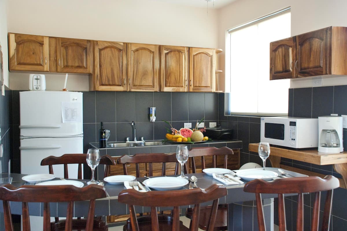 A kitchen with wooden cabinets, a refrigerator, a microwave, and a dining table set with plates and glasses.