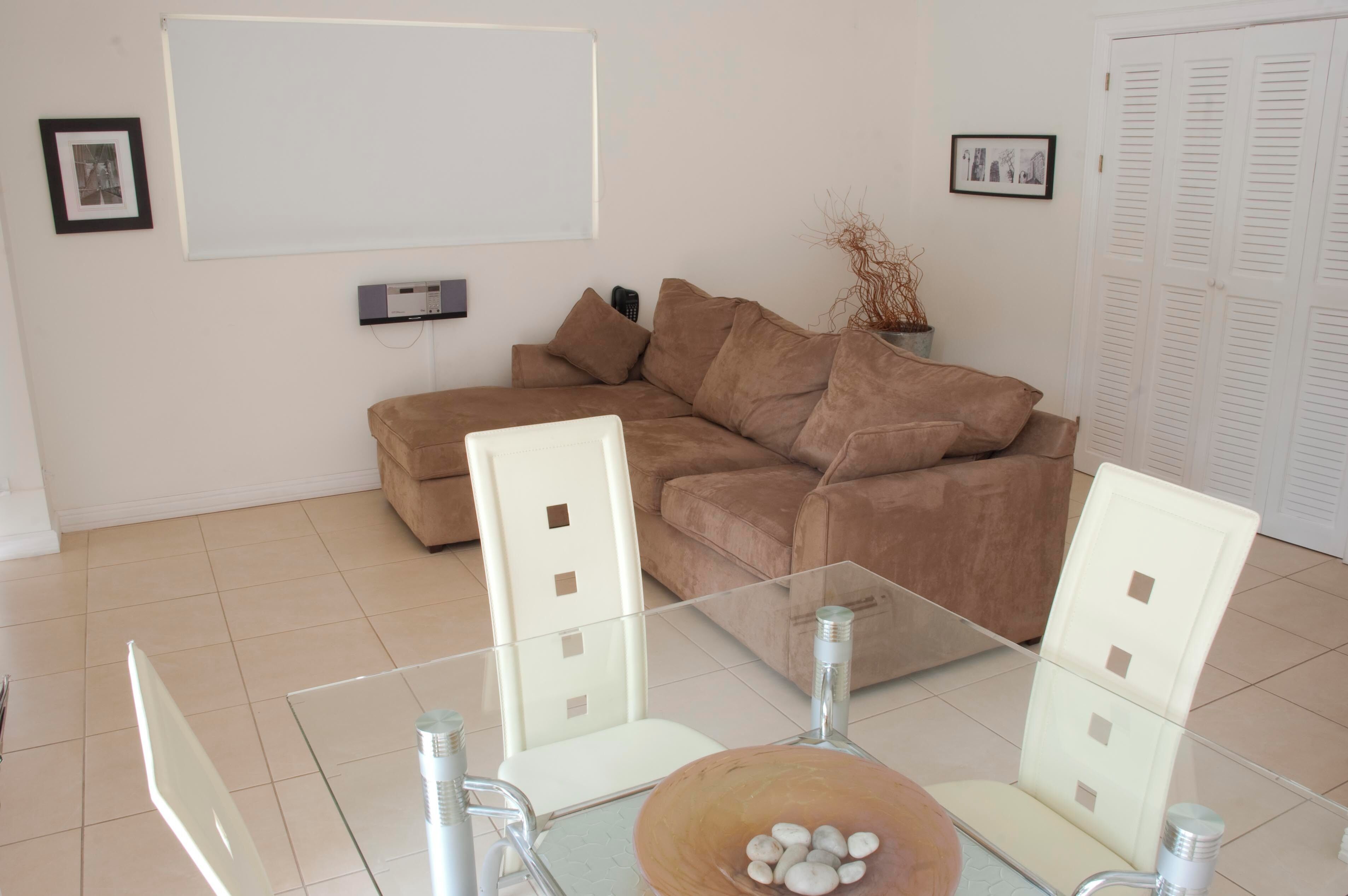 A modern living room with a beige sectional sofa, a glass coffee table, and white chairs.