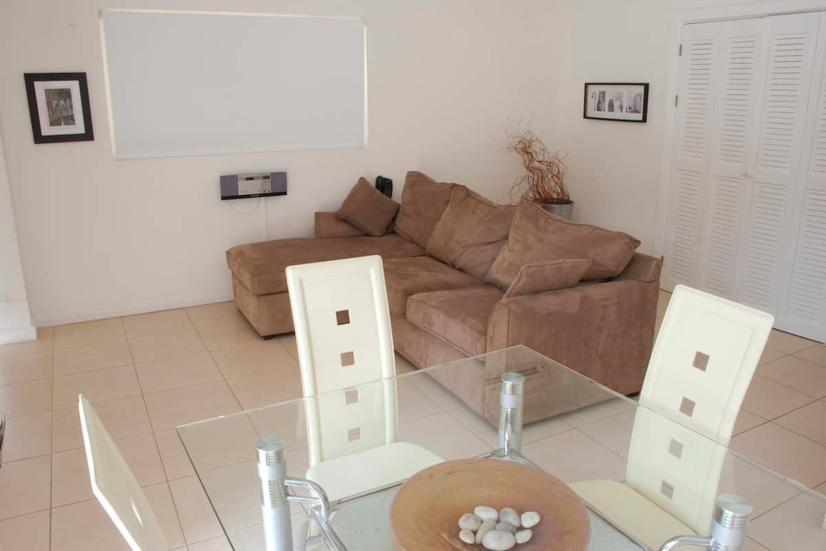 A modern living room with a beige sectional sofa, a glass coffee table, and white chairs.