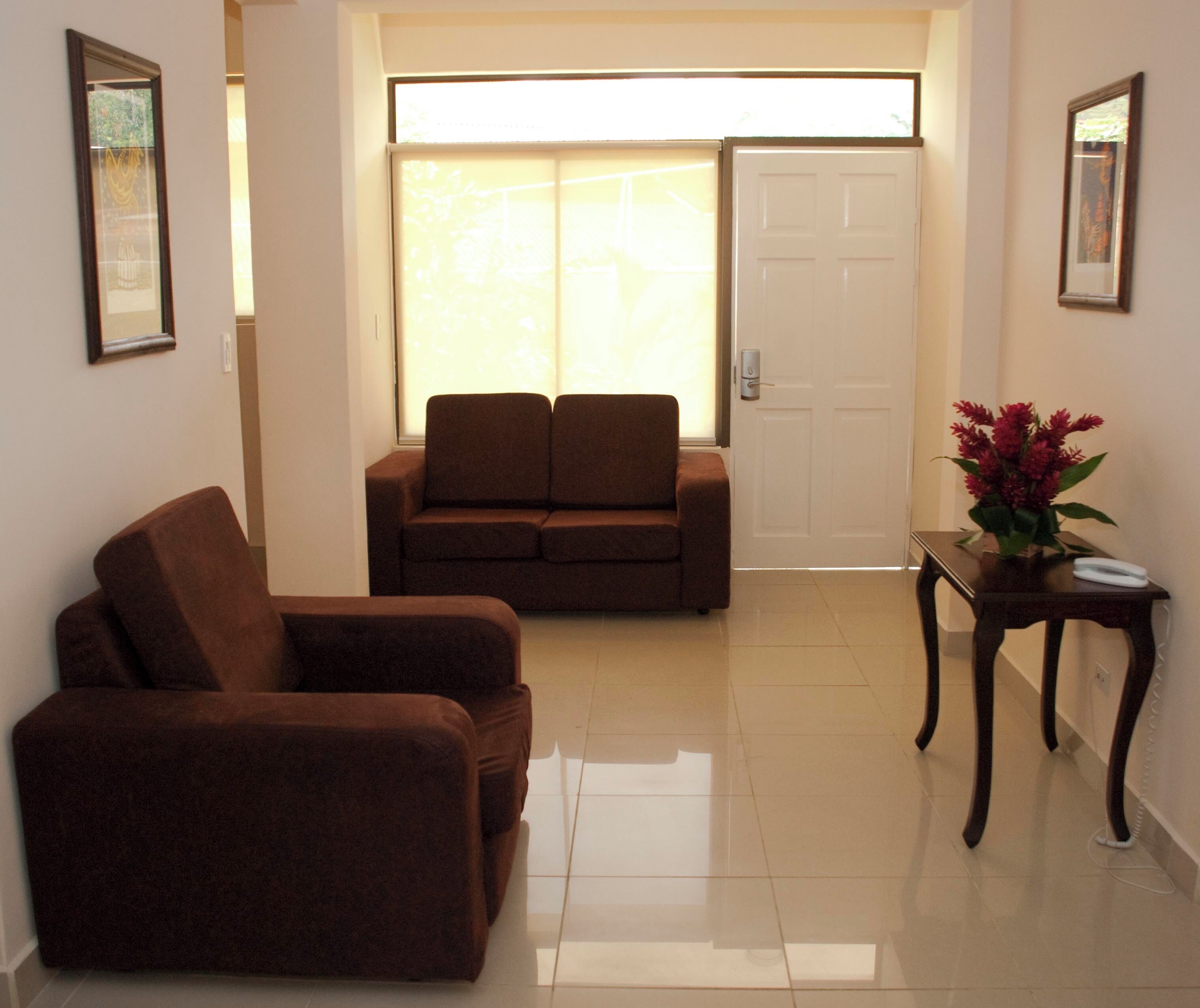 A room with a sofa, a chair, a table with a vase, and a door.