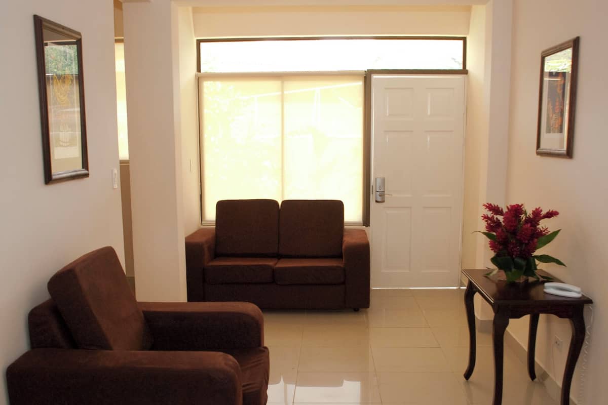 A room with a sofa, a chair, a table with a vase, and a door.