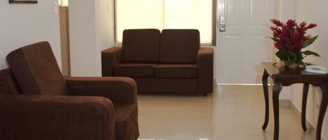 A living room with a brown sofa, a small table with a vase, and a door with a view to the outside.