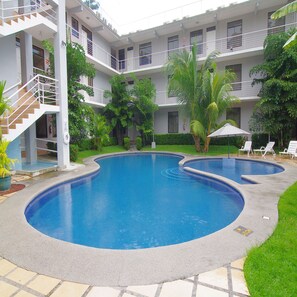 Una piscina de diseño curvo, rodeada por un edificio blanco con varios balcones y una escalera.