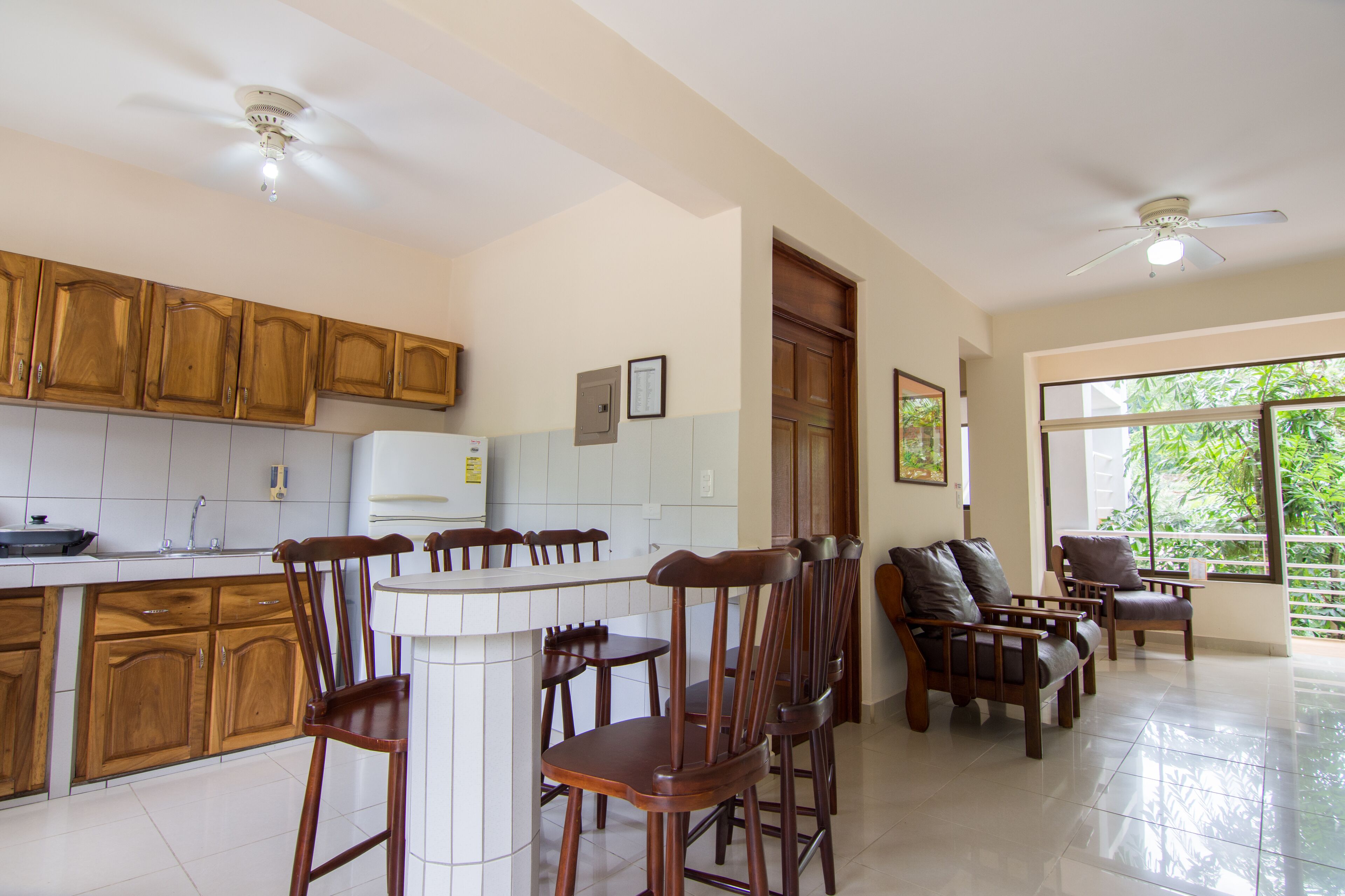 Cocina con armarios de madera, encimera blanca y comedor con sillas de madera y un sofá.