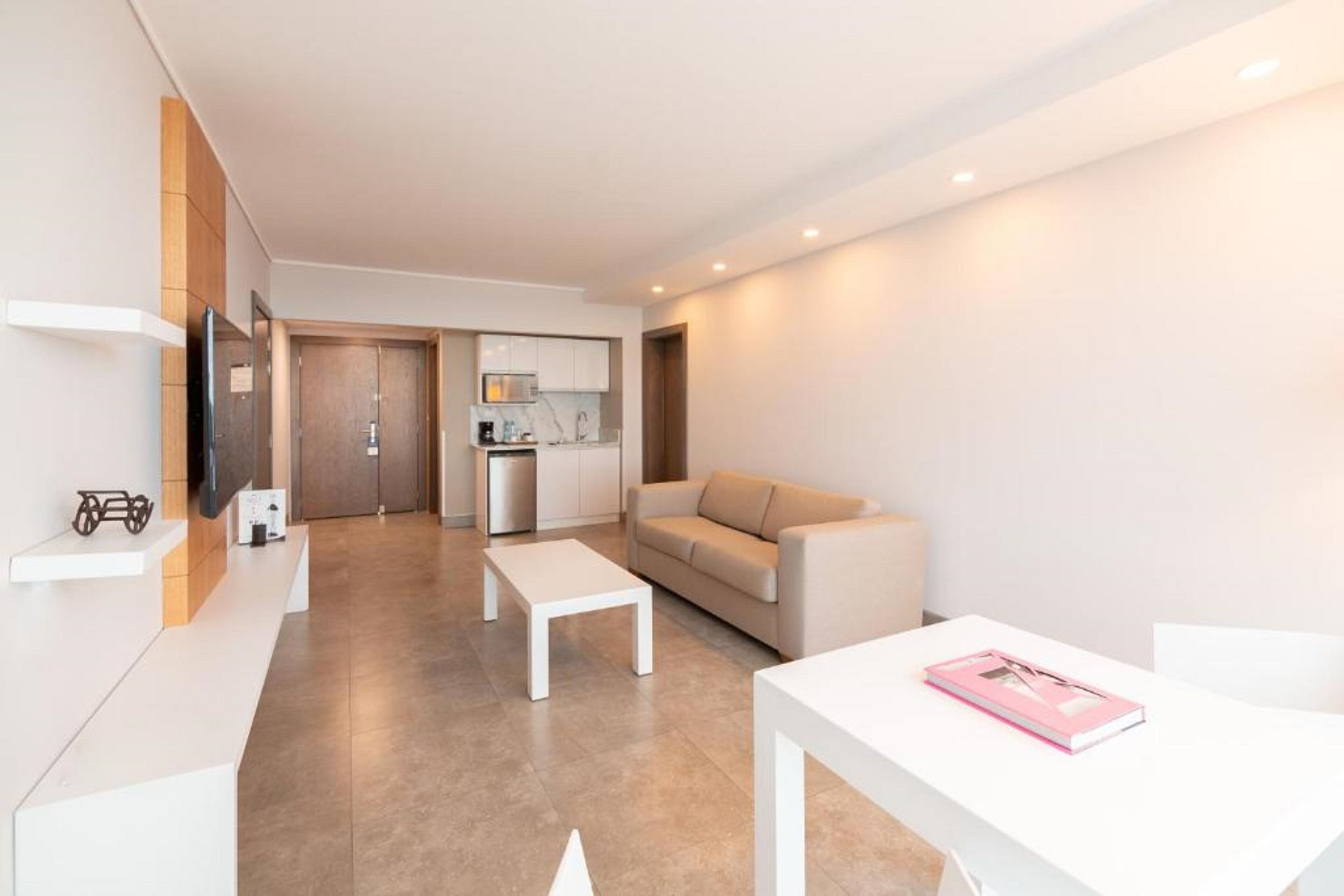 A modern, minimalist living room with a sofa, coffee table, and a small kitchen area in the background.