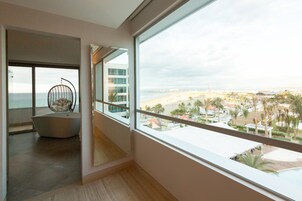 Une chambre d’hôtel moderne dotée d’un grand balcon, offrant une vue sur la plage, et comprenant un fauteuil unique.