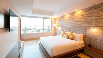 A modern bedroom with a large bed, a mounted TV, a city view, and a wooden accent wall.