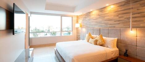 A modern bedroom with a large bed, a mounted TV, a city view, and a wooden accent wall.