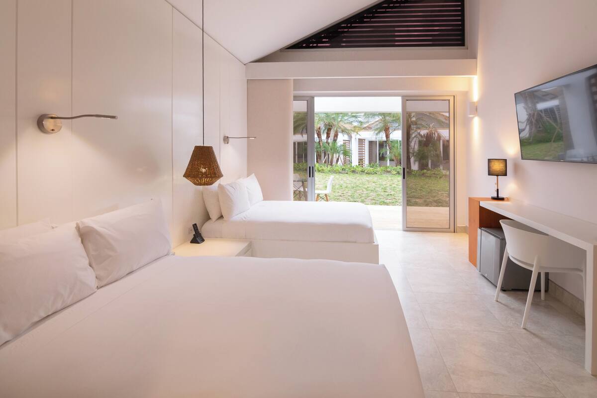 Una habitación de hotel moderna con dos camas, un escritorio y una puerta corrediza de vidrio que da a un jardín.