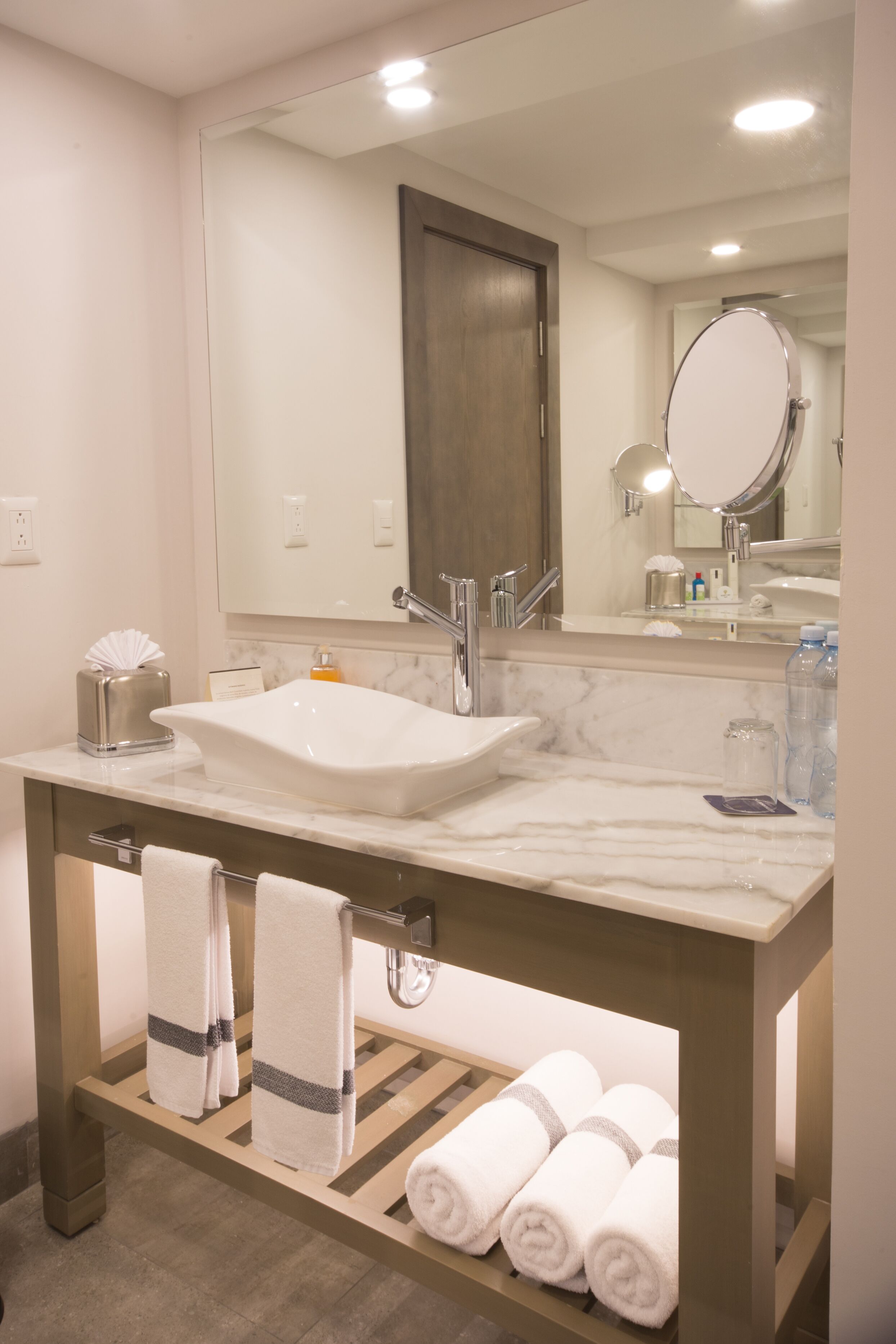 A bathroom with a marble sink, a large mirror, and a towel rack with towels.