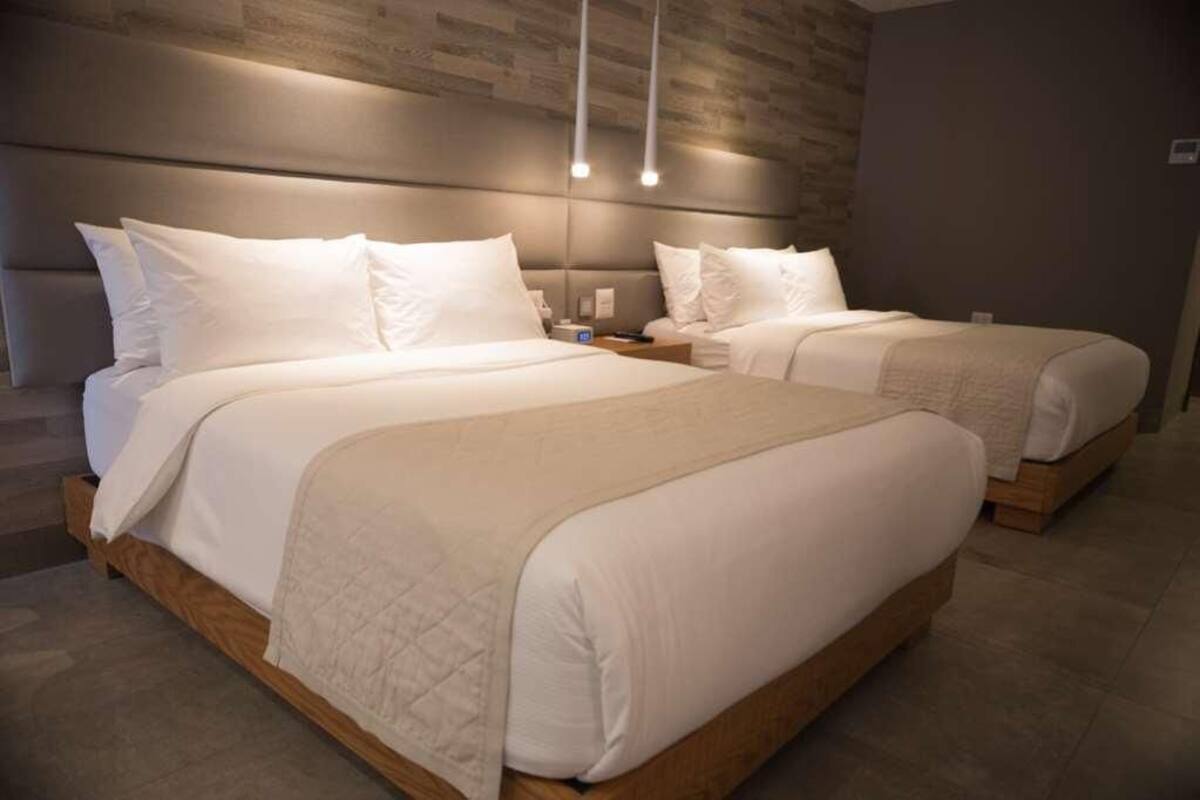 Habitación de hotel con dos camas, cabecero de madera y una lámpara moderna.