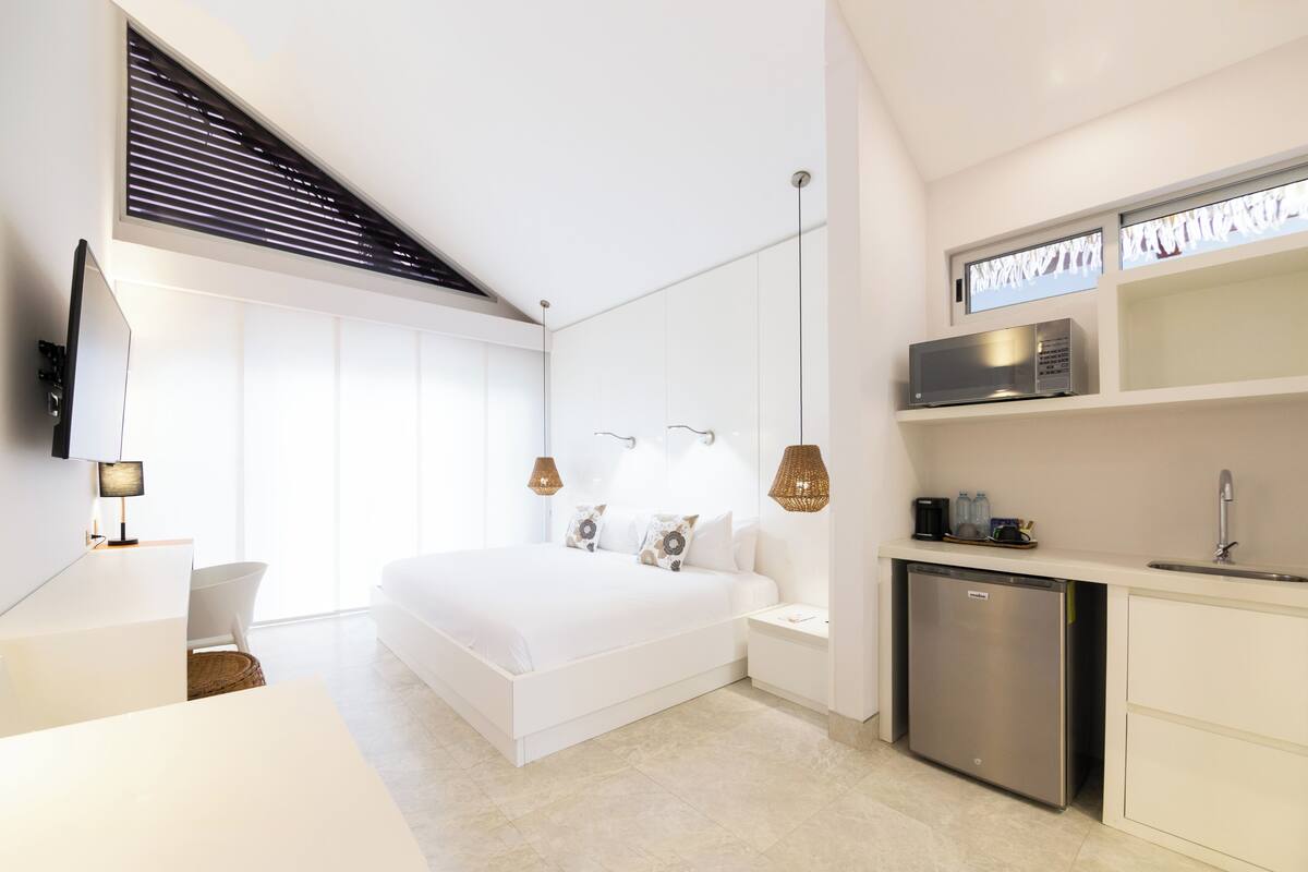 Un dormitorio moderno con una cama grande, mesitas de noche, televisor integrado y una pequeña cocina con microondas.